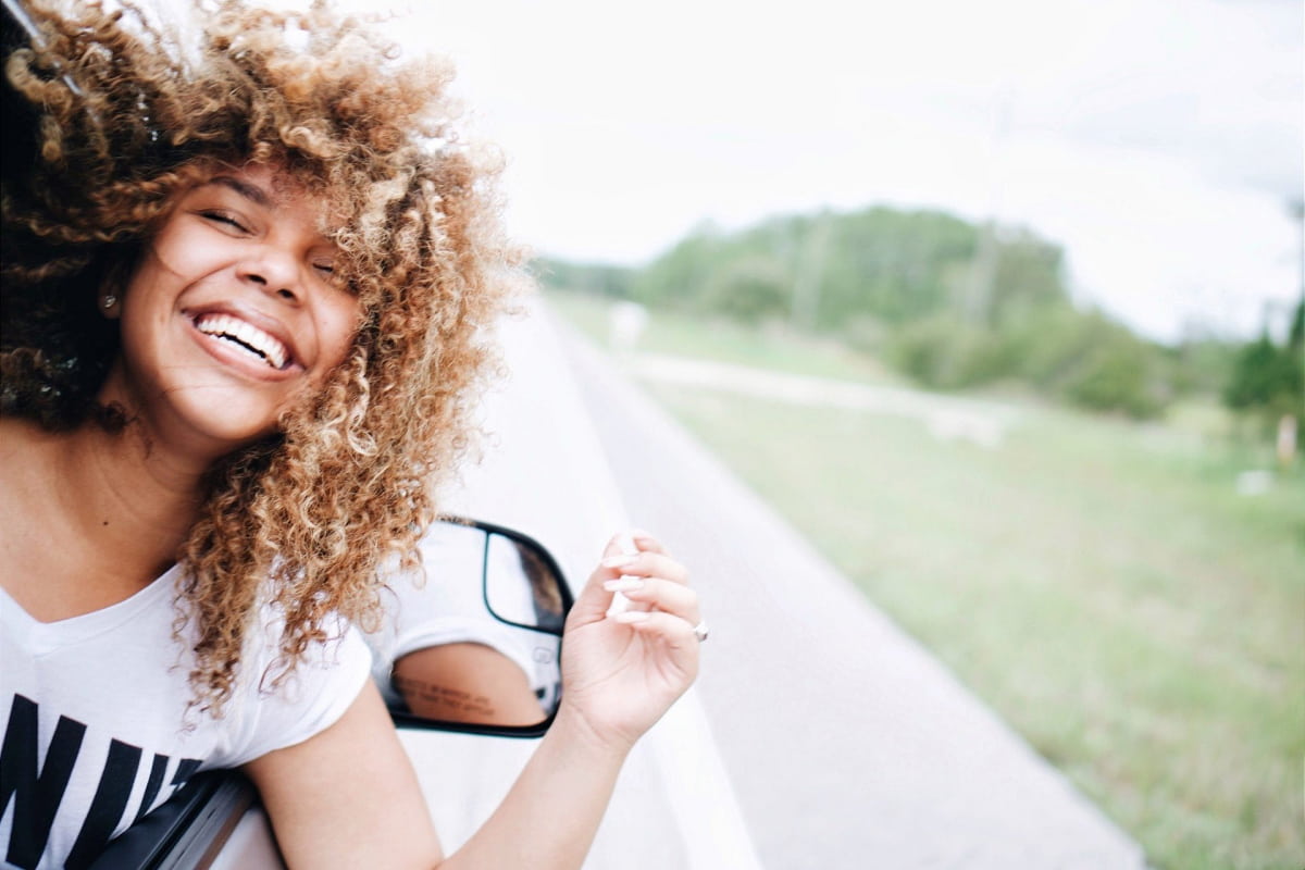 curly haired woman with head out car smiling eyes closed