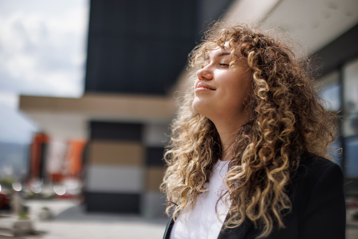 Business woman with long curly hair outside smiling eyes closed