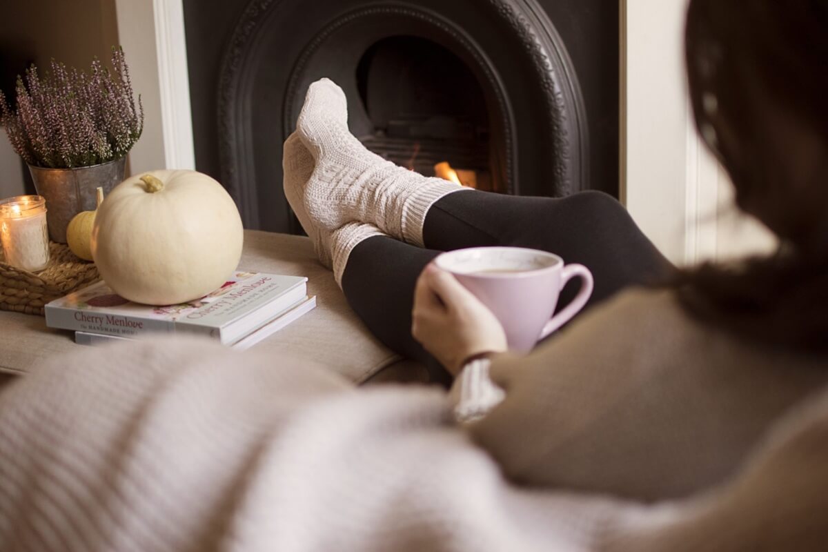 woman reduces stress drinking cocoa with feet next to fireplace