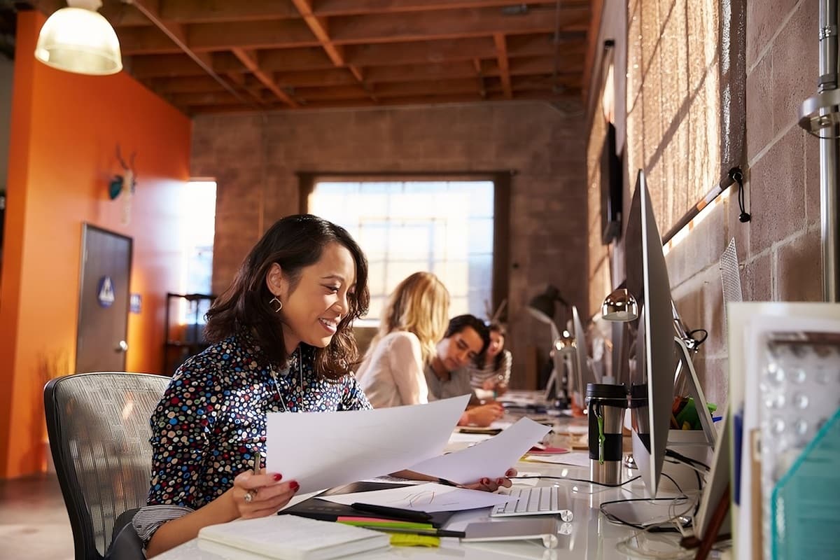 Asian female employee working by computer holding print outs