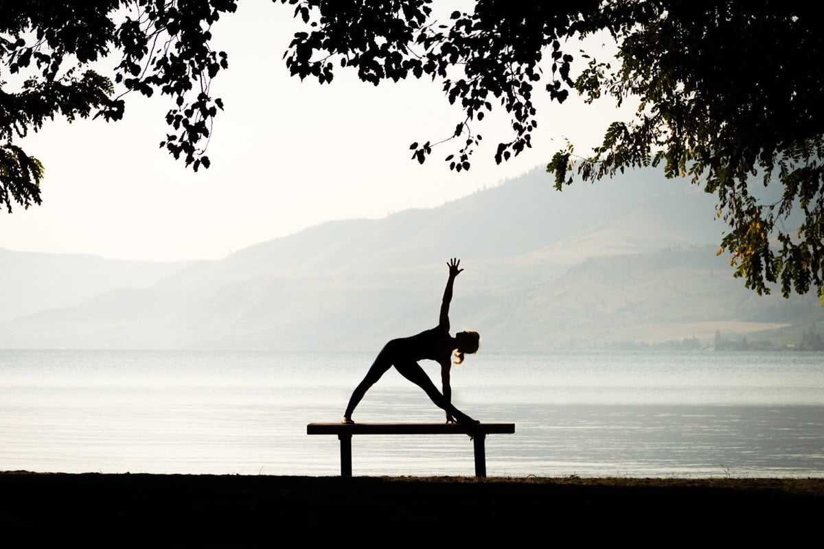 silhouette of woman doing yoga pose on bench in front of lake