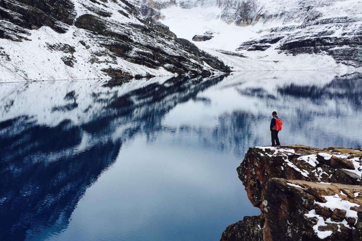 Man standing on cliff looking as clear water and mountains