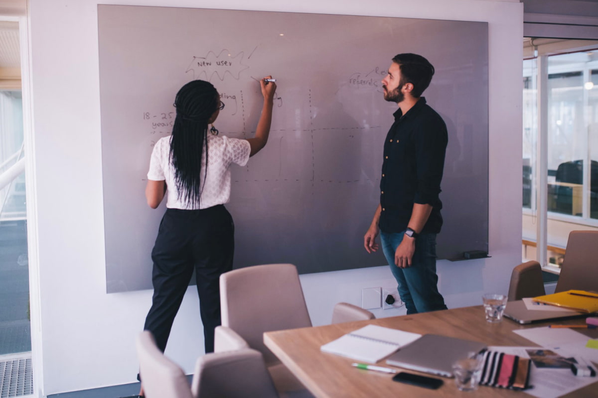 Woman writing on whiteboard with man watching in the office