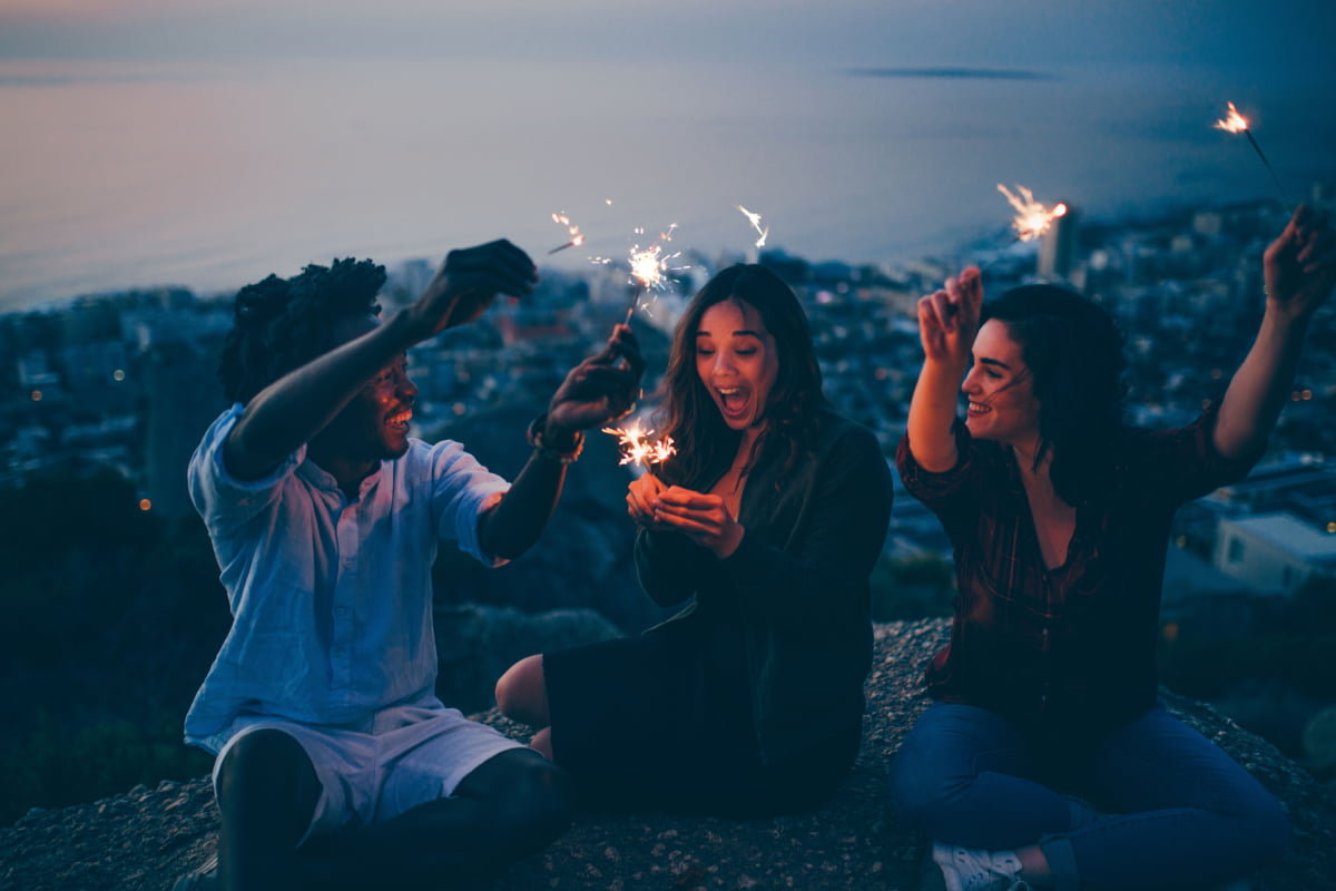 Three young people sitting outside holding sparklers and laughing