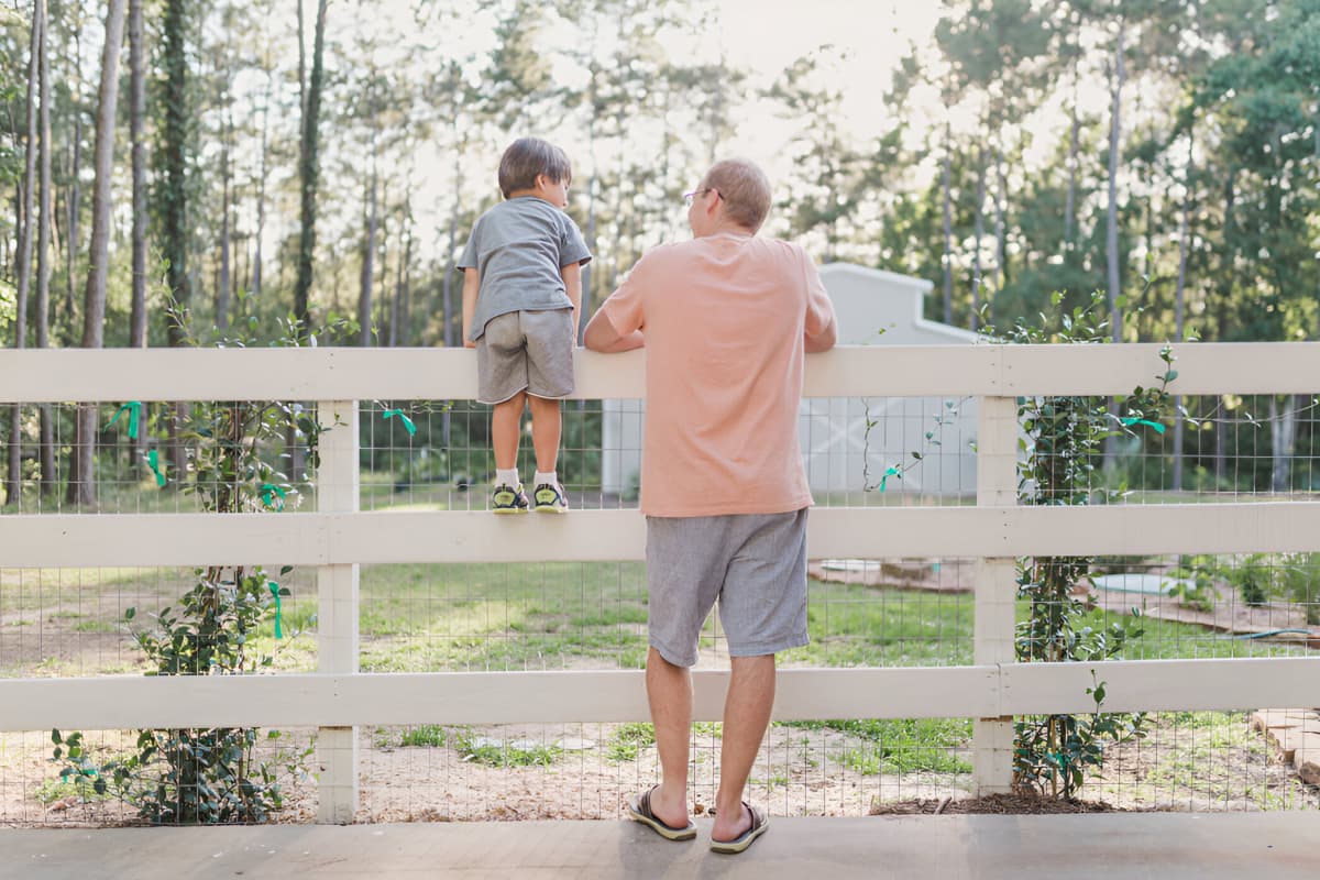 Father and young son leaning on wooden fence