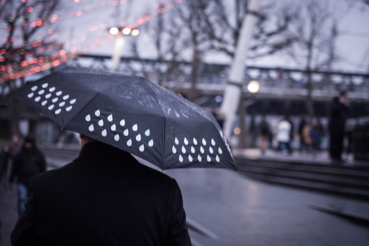 Man holding umbrella walking in city getting dark