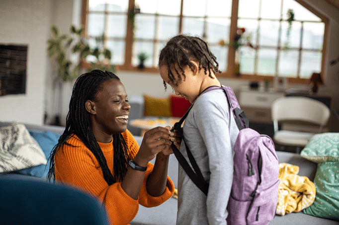 african american mom putting backpack on daughter for school