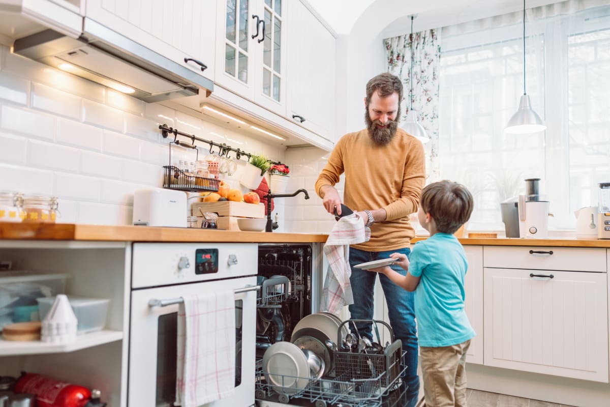 Little son helping bearded father in kitchen with drying dishes