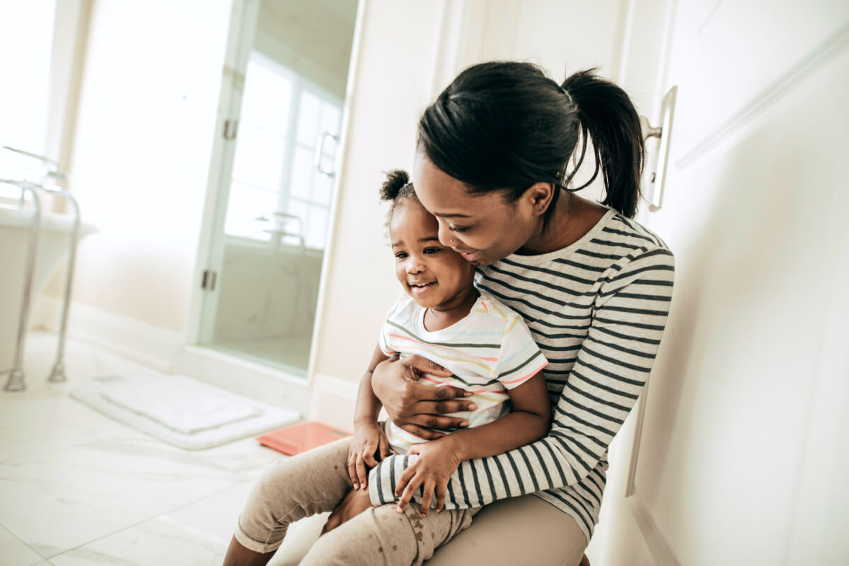 African American mother potty training toddler daughter in bathroom