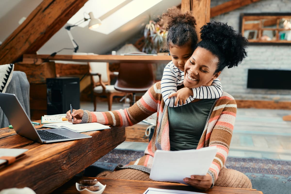 Happy African American mother working from home while ADHD daughter embraces her