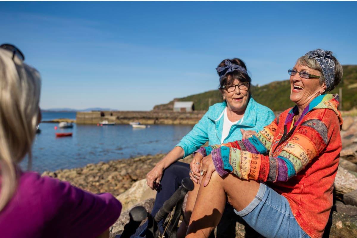 senior women sitting and chatting on rocks by ocean